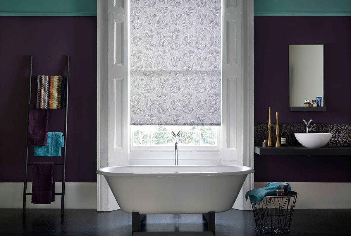 Modern bathroom with dark plum walls and sash windows dressed with grey pattern roller blind