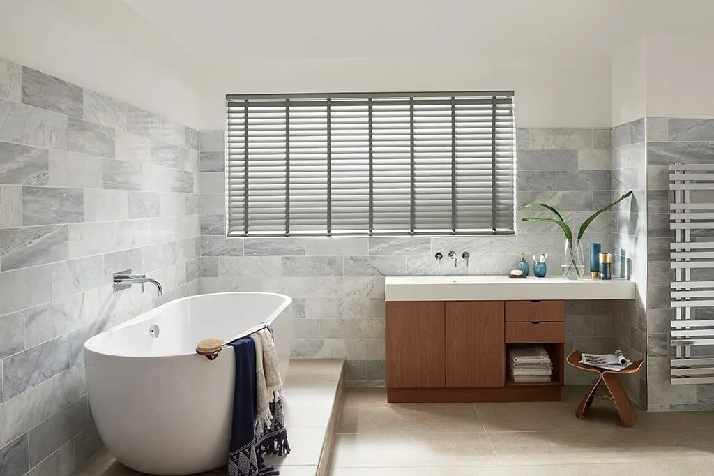Modern luxe bathroom with white ceramic tub and grey Venetian blinds