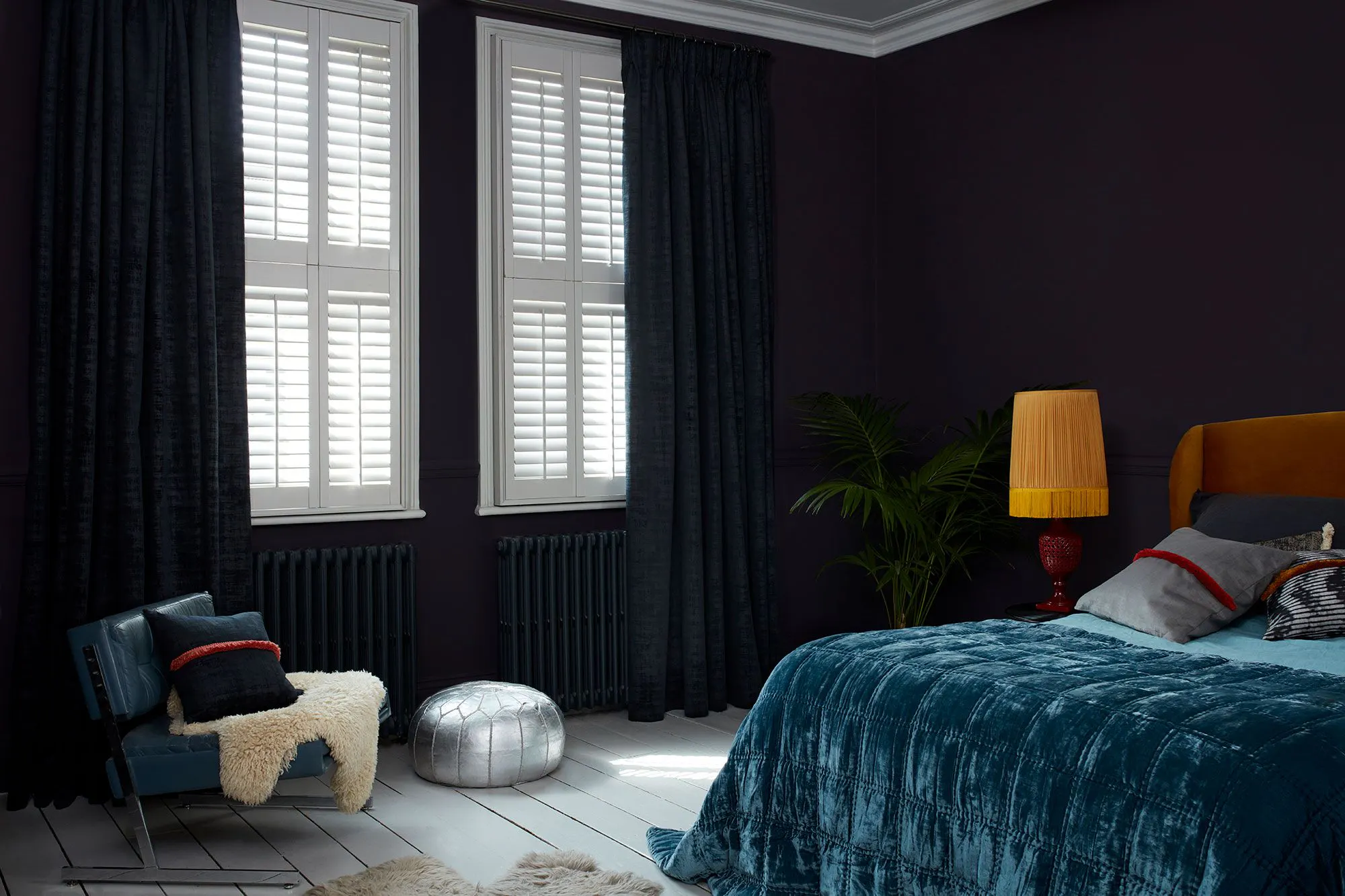 Black coloured cley mole curtains matched with white tier on tier shutters in a bedroom decorated with navy blue walls.