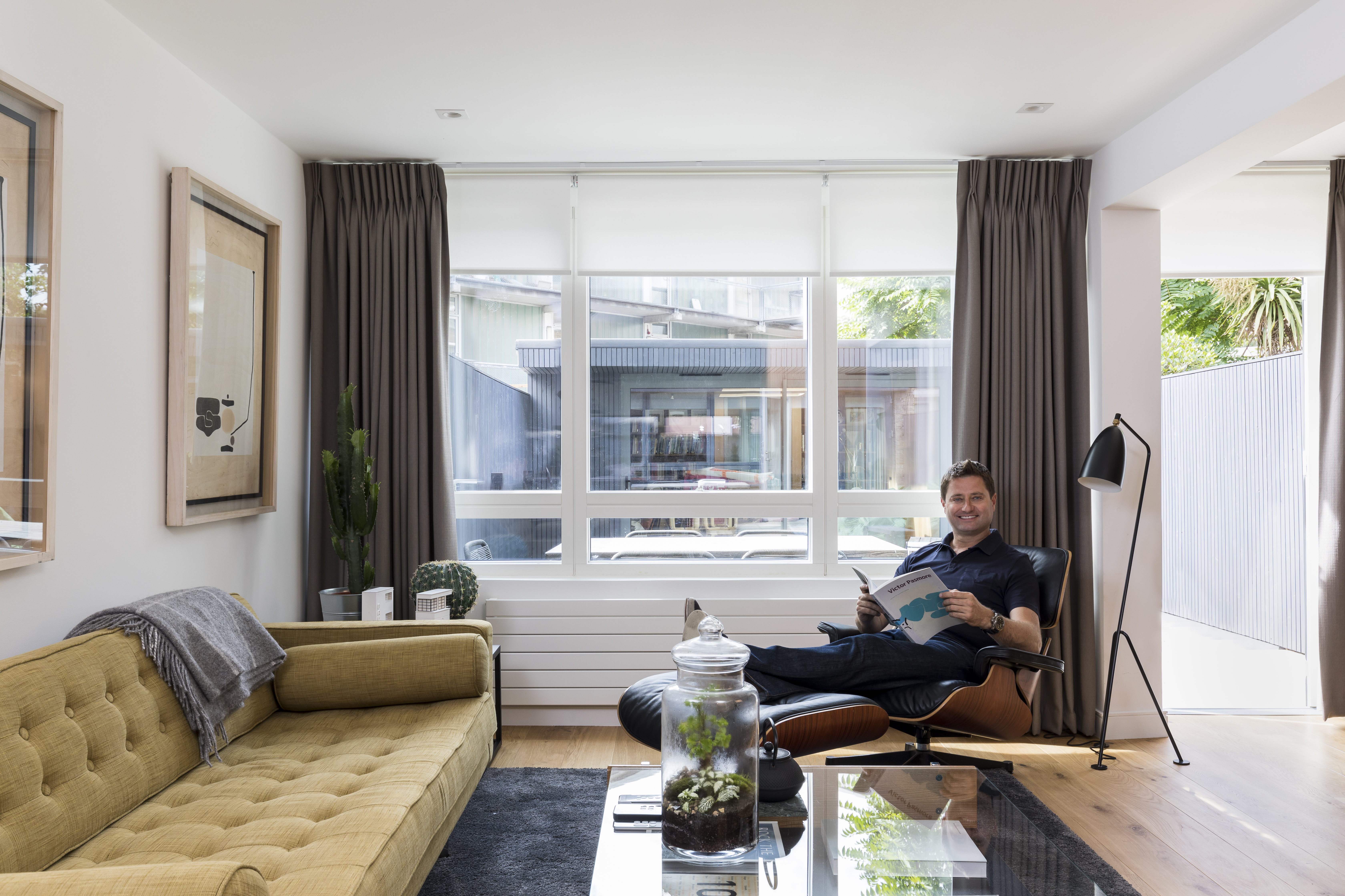 Modern living room with grey motorised roller blind and Bardot grey curtains, featuring a neutral color palette and soft, ambient lighting.