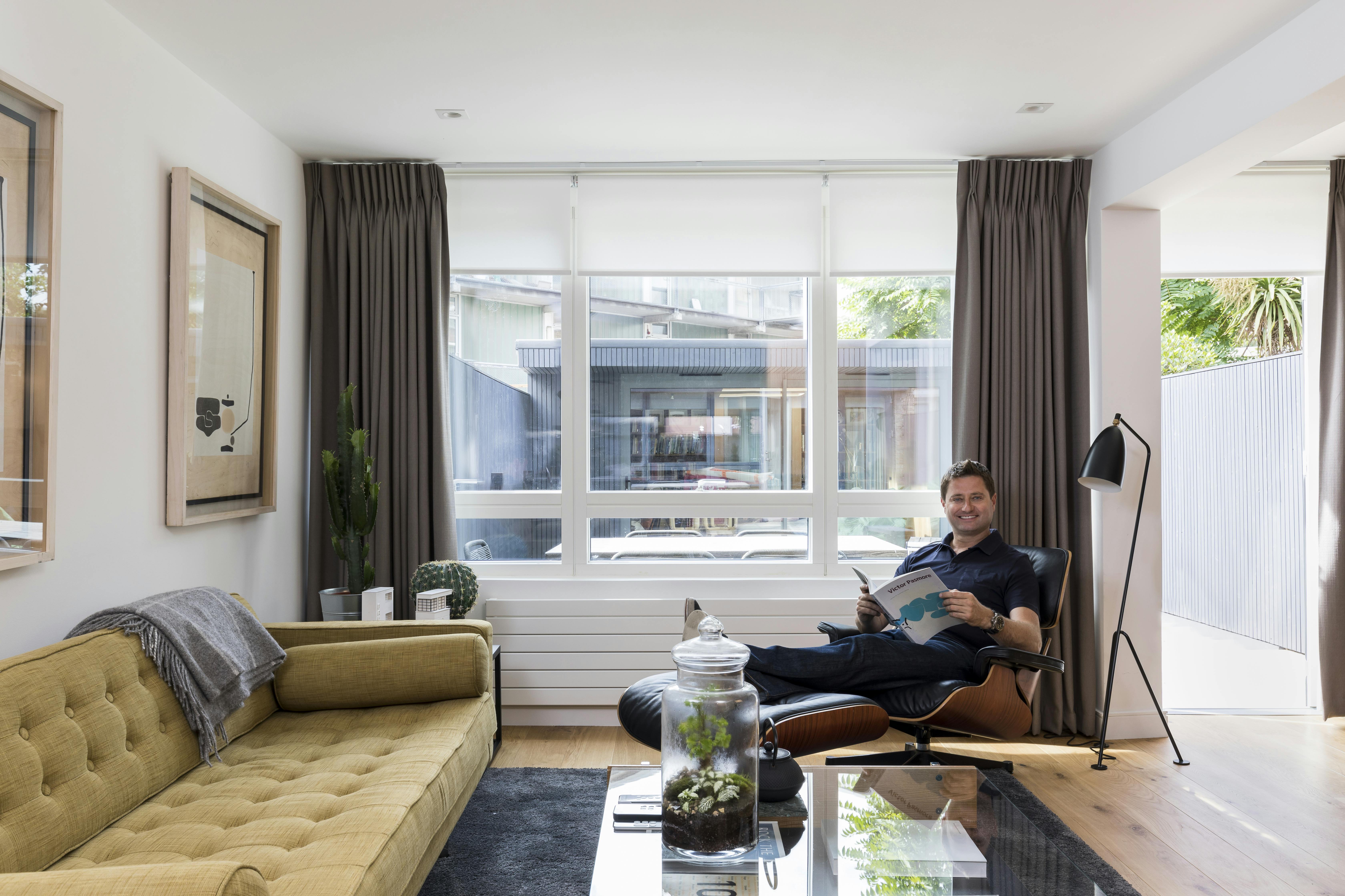 Modern living room with grey motorised roller blind and Bardot grey curtains, featuring a neutral color palette and soft, ambient lighting.