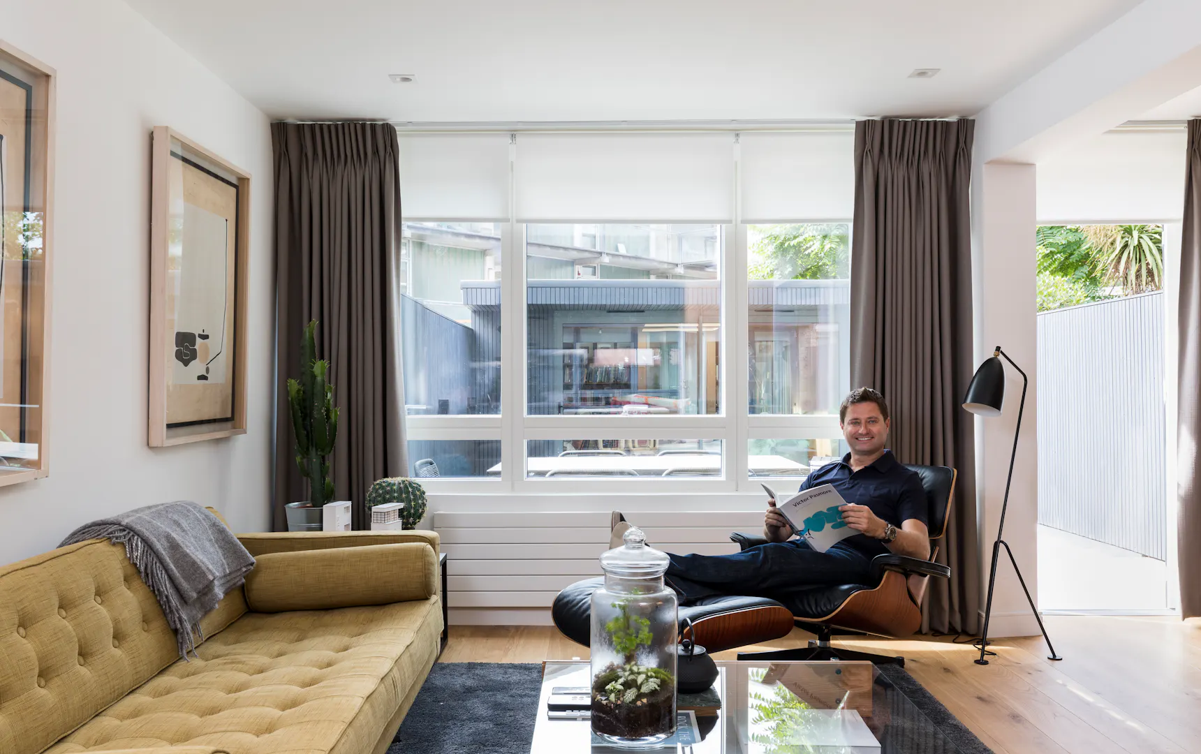 Modern living room with grey motorised roller blind and Bardot grey curtains, featuring a neutral color palette and soft, ambient lighting.