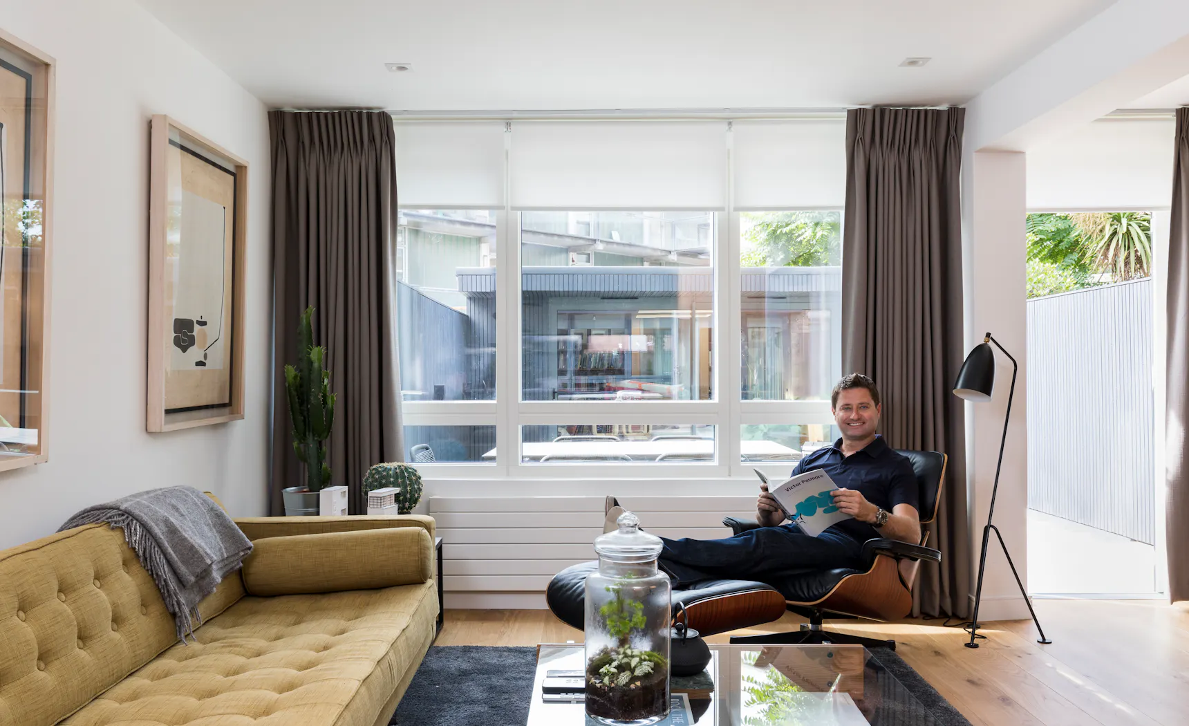 Modern living room with grey motorised roller blind and Bardot grey curtains, featuring a neutral color palette and soft, ambient lighting.