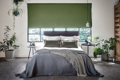 Modern bedroom with green blackout roller blind, grey bedding, and indoor plants, creating a calm, nature-inspired atmosphere.