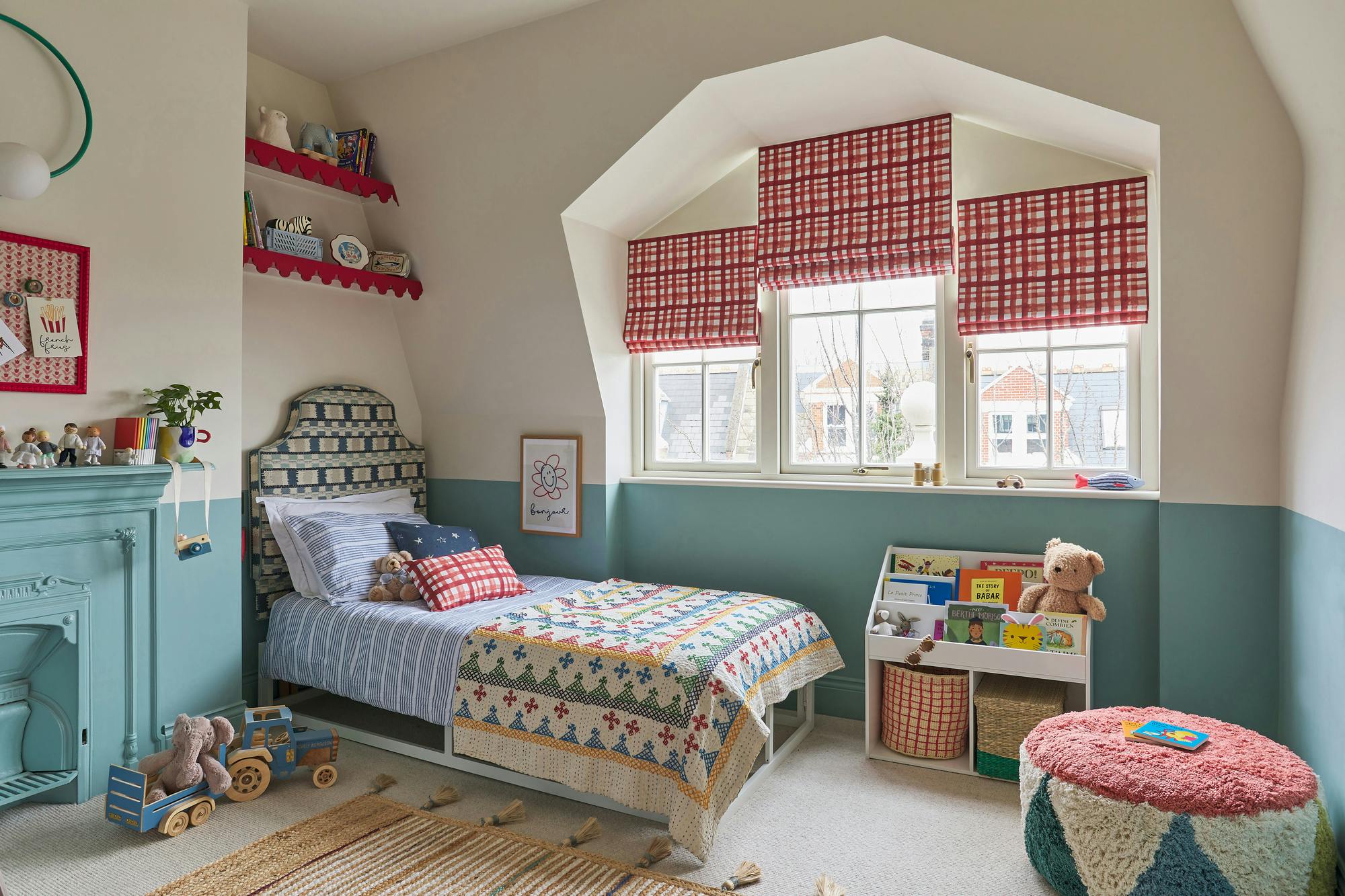 Kids bedroom in cream with lower half walls in mid dusky blue, white and blue striped bedding, red edges to shelf and pinboard and inset windows dressed in three red and white checked Roman blinds.