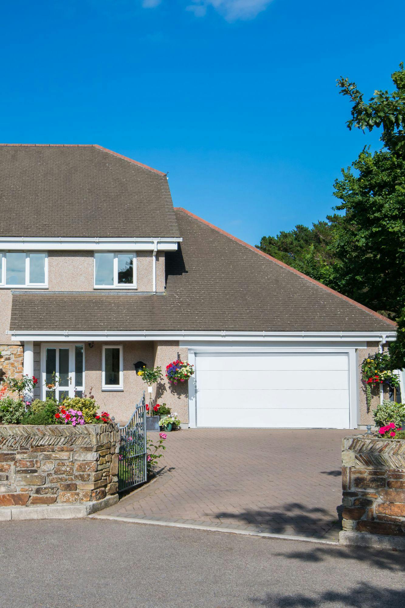 60s-style property in floral setting with dormer integral garage with white sectional garage door and matching front door.