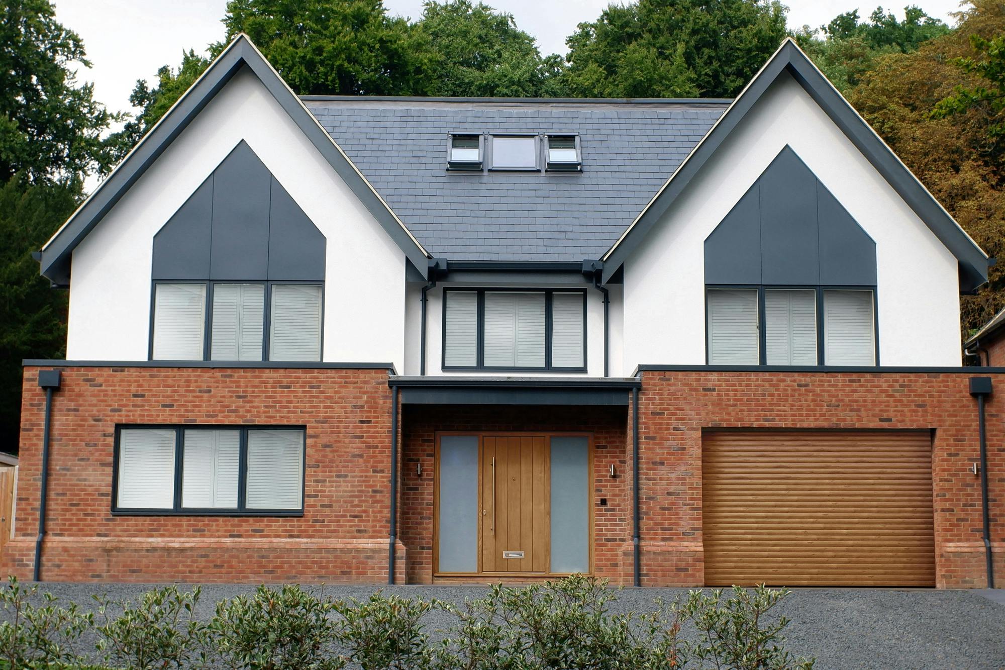 Large contemporary two-tone house with apex windows and integral garage with light brown door matching front door.