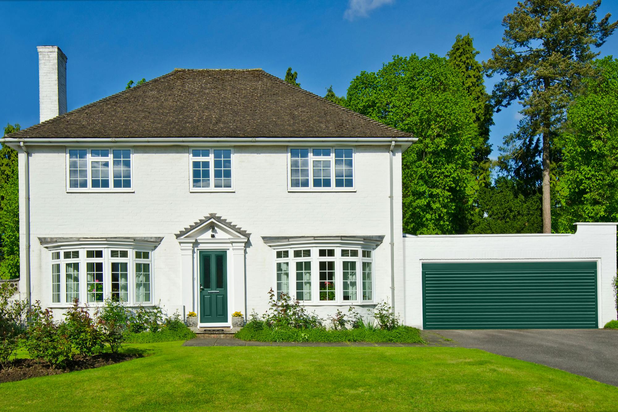 Large white house with bay windows, green door and attached garage in matching white with green door, lawn to front.