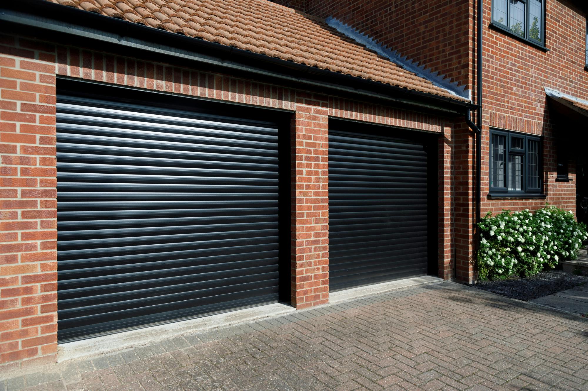 Close up of modern brick property with attached double garage with garage doors in dark grey.