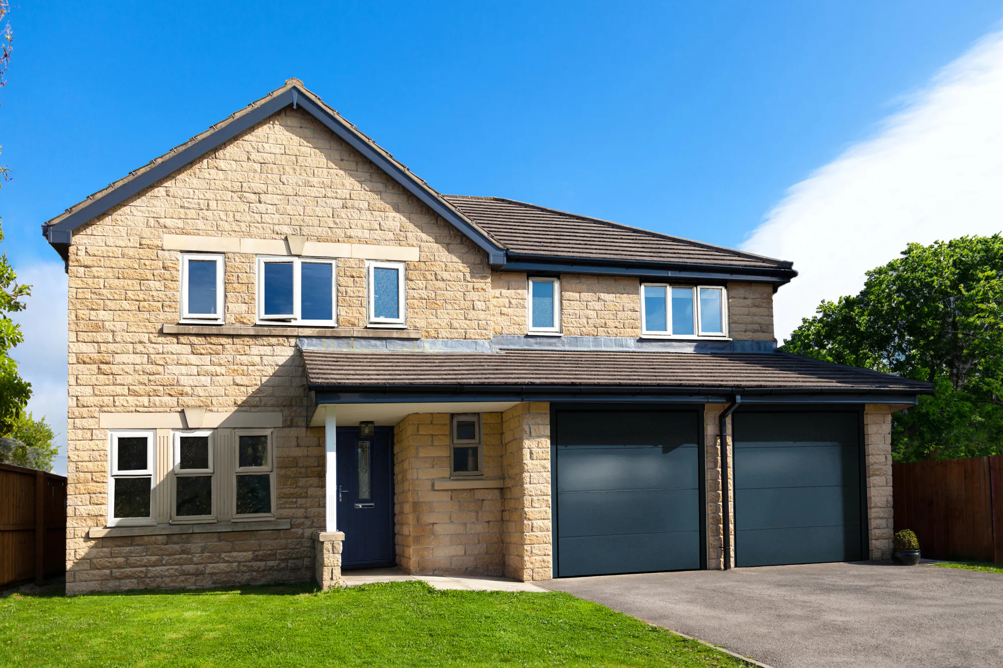 Yellow Cotswold stone-style house with integral garage with two blue steel garage doors that match the front door.