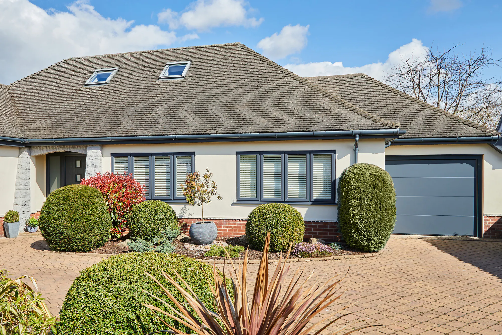 Single storey house in white with anthracite grey integral garage door matching guttering and window frames and block paved driveway.
