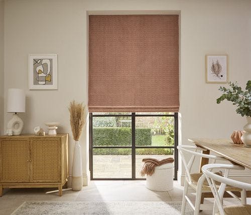 Bright dining area with blush pink Roman blind, natural wood furniture, modern art, and neutral decor creating a warm, inviting atmosphere.