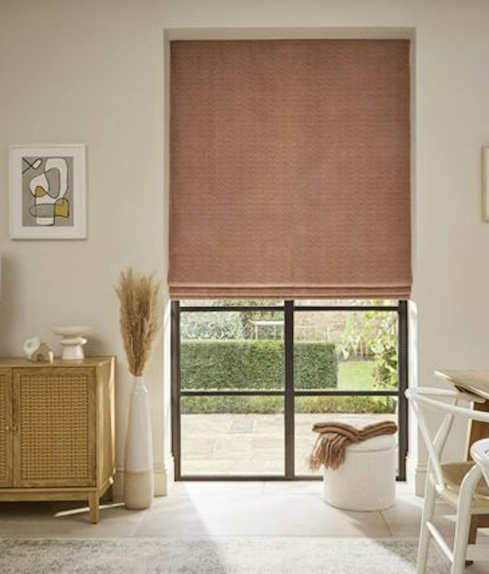 Bright dining area with blush pink Roman blind, natural wood furniture, modern art, and neutral decor creating a warm, inviting atmosphere.