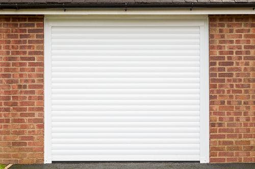 Closed white roller garage door set in a red brick wall with a black shingle roof and a clean, simple exterior design.