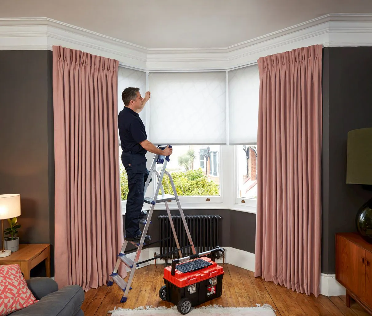 Friendly Hillarys advisor with branded uniform helping to fit white blinds in customer's home