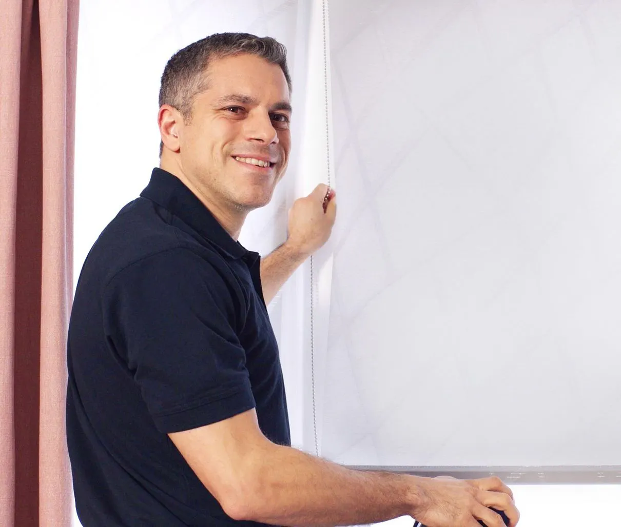 Hillarys advisor smiling while fitting white roller blinds on a window