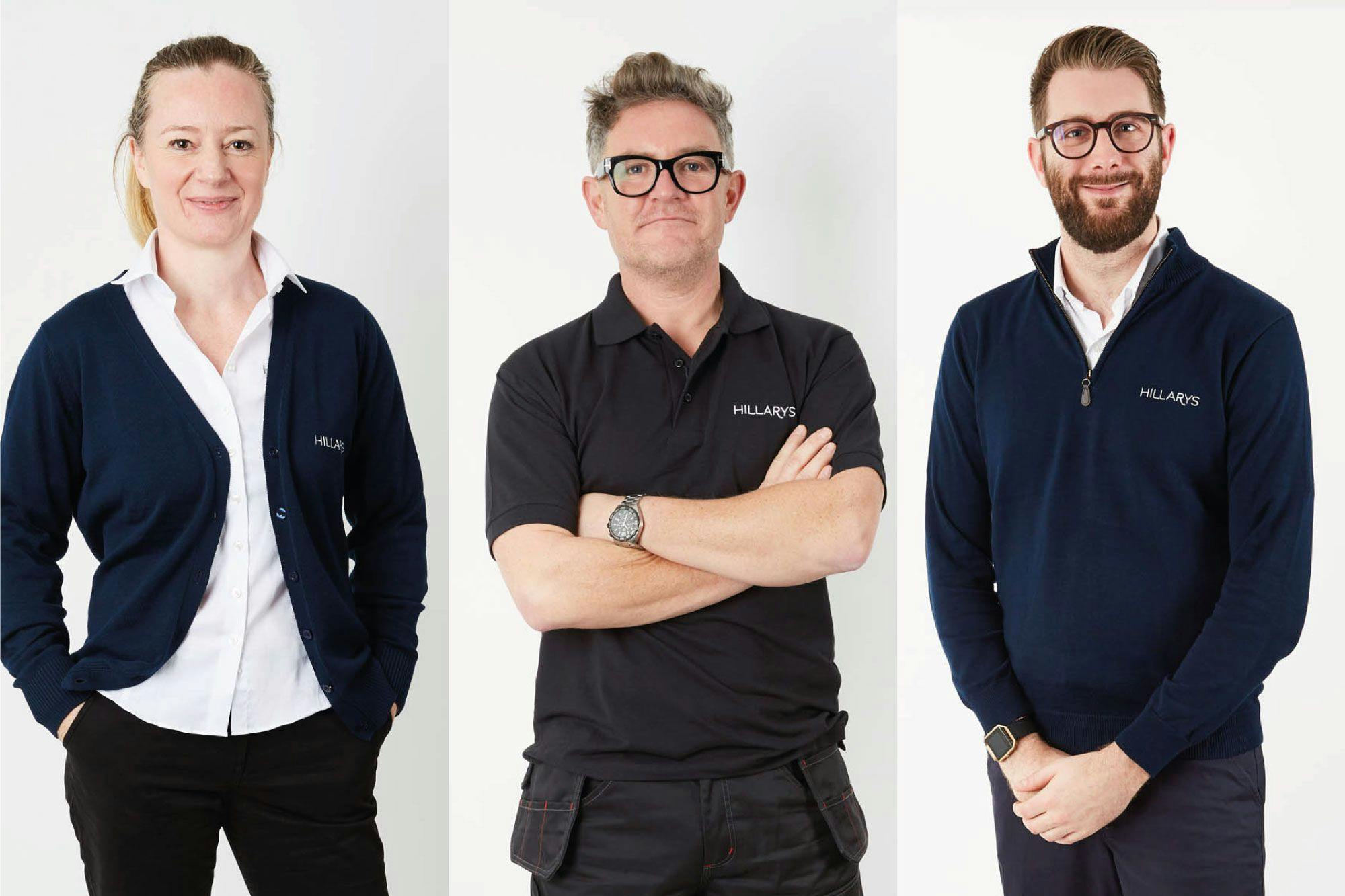 Three Hillarys advisors wearing branded navy uniforms, standing side‑by‑side against a white studio backdrop.