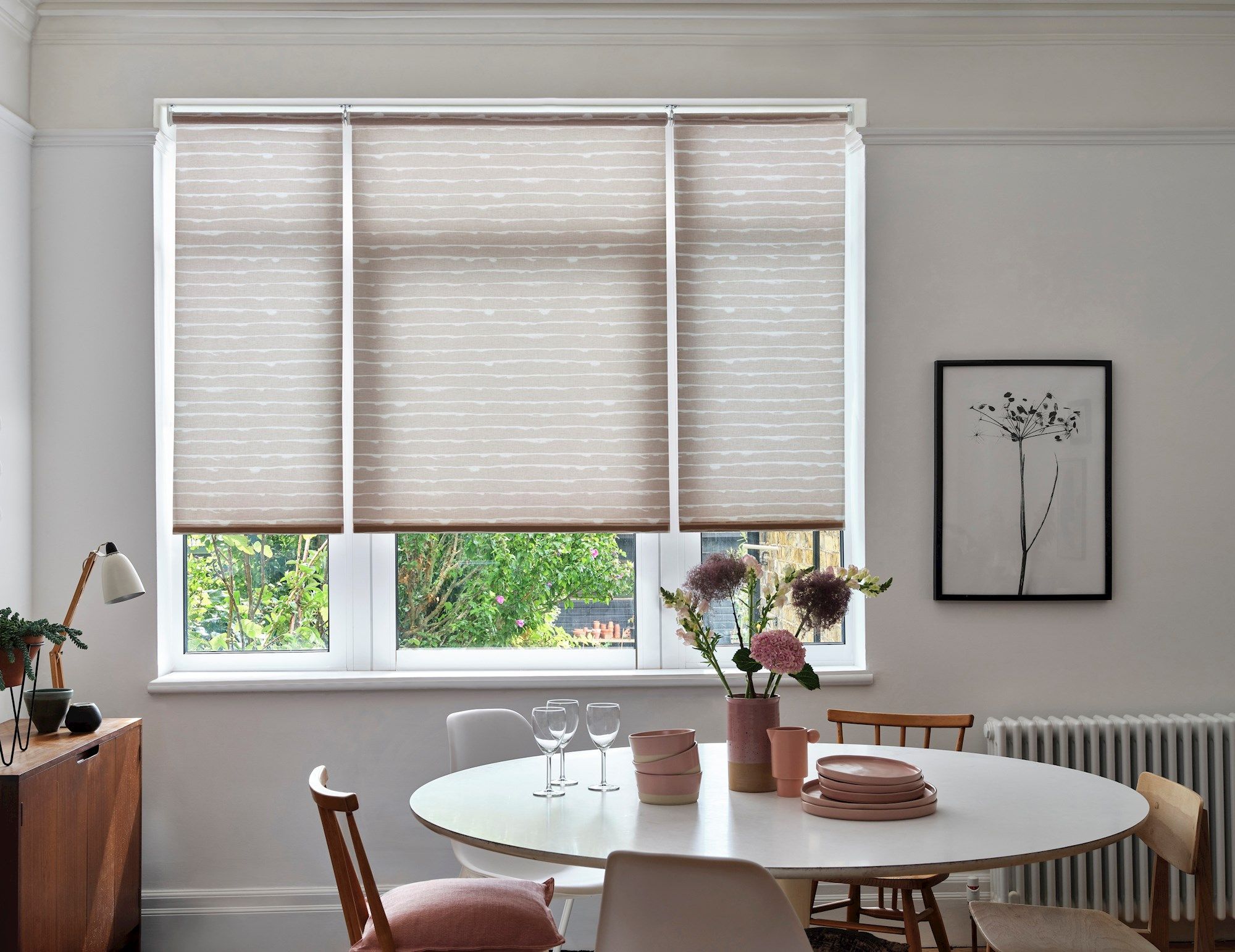 A neutral dining room with light grey and white striped blinds and modern, wooden furnishings