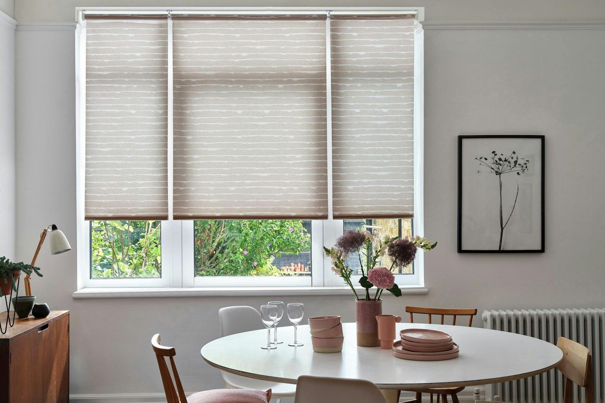 A neutral dining room with light grey and white striped blinds and modern, wooden furnishings