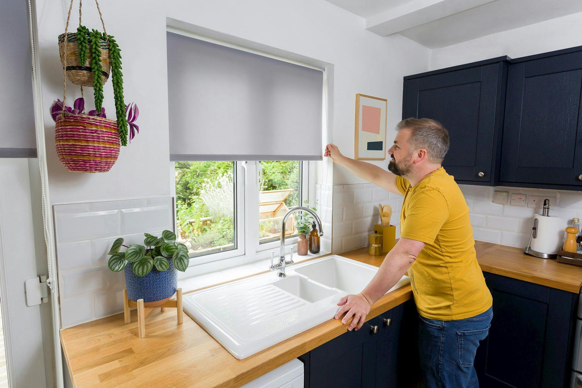 User-generated shot of a modern kitchen: pale-grey roller blind half-lowered above a sink, with leafy garden view beyond the window.