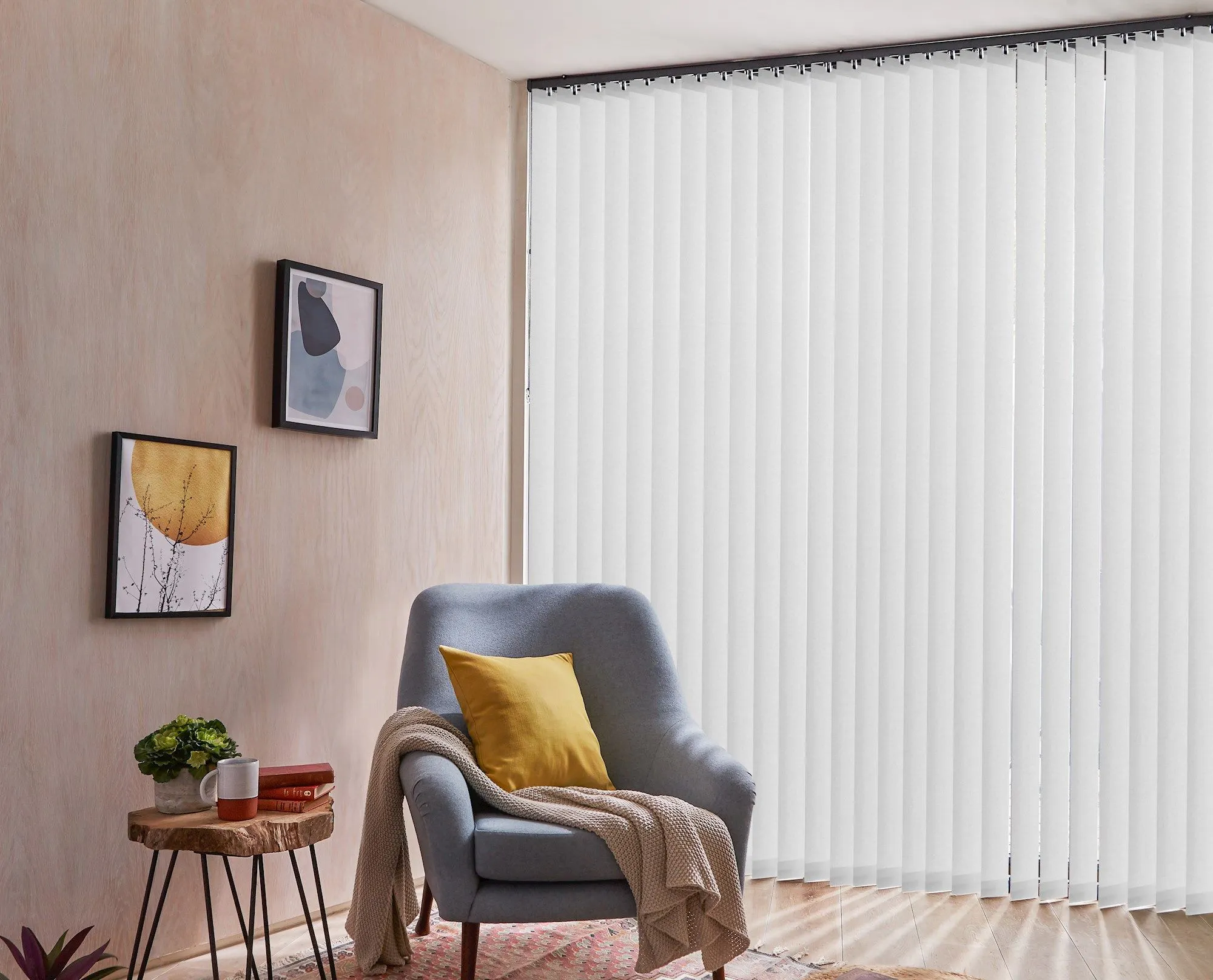 Light‑grey vertical blinds spanning a living‑room bay window beside a blue sofa and glass coffee table.