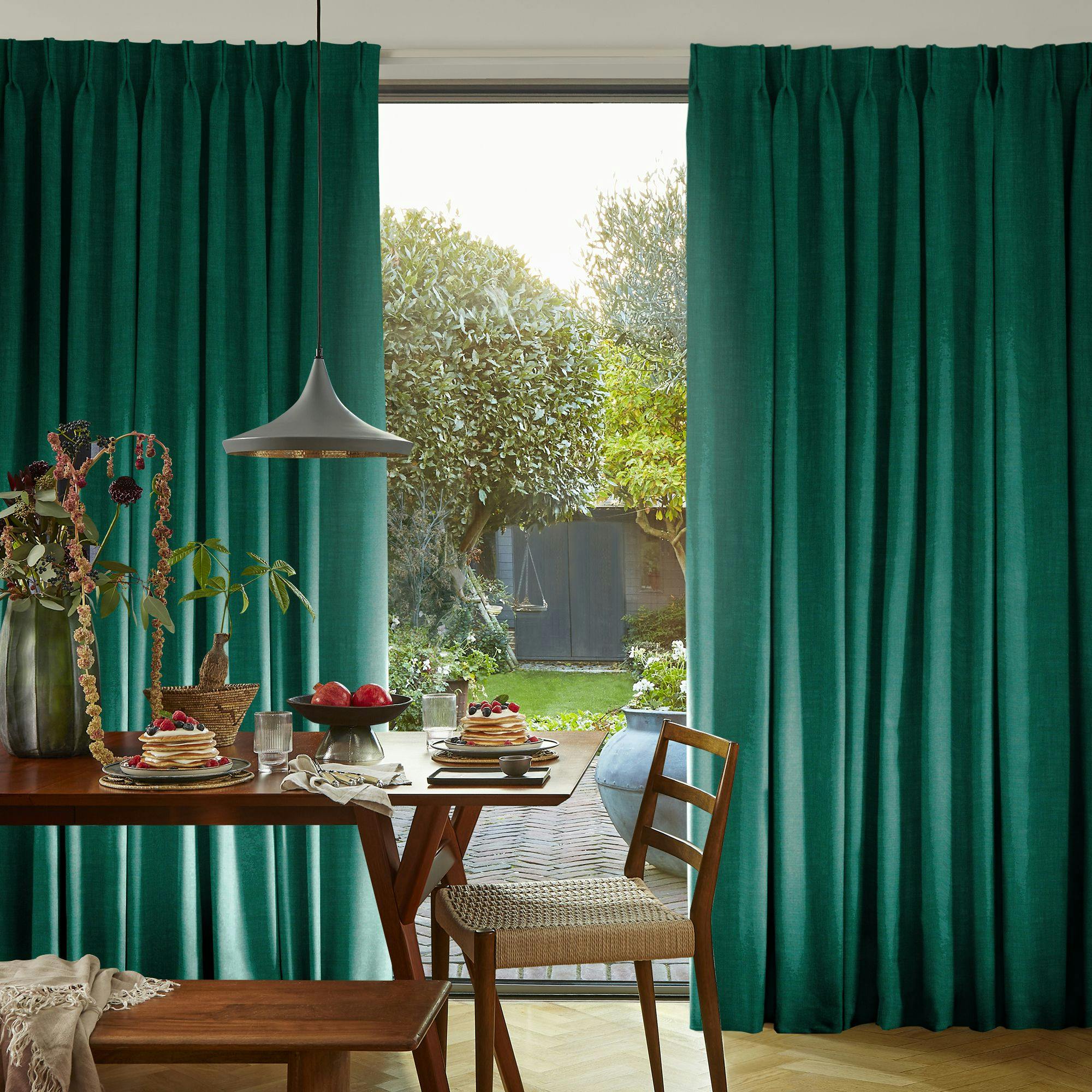Deep teal curtains drawn across full‑height garden doors behind a wooden dining table laid for dinner.