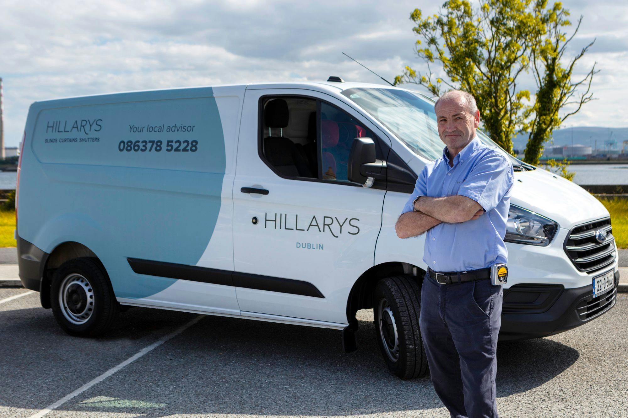 Hillarys advisor smiling beside the two-tone blue company van, ready for an at-home appointment.