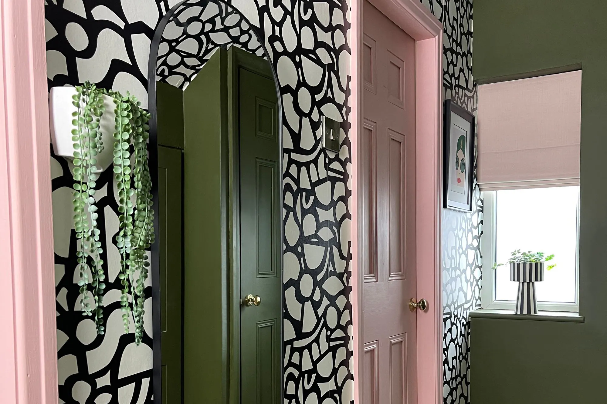 Room with rear wall in olive green, doors and paintwork in baby pink, walls and ceiling in white with black organic irregular bubble print design, cream floor with painted rug design in olive with chevron pattern.