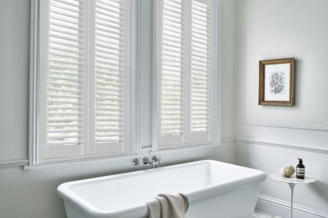 White vinyl shutters on windows in a modern light bathroom