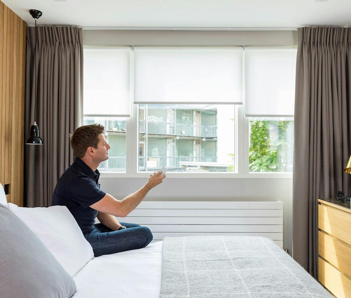 Modern bedroom with grey motorised roller blind and Bardot grey curtains, featuring a neutral color palette and soft, ambient lighting.