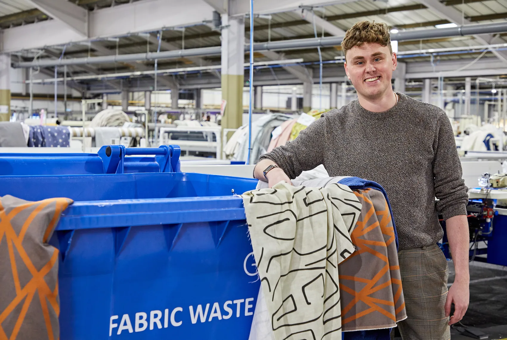 Sam culter, head of sustainability standing holding fabrics in front of a fabric waste bin
