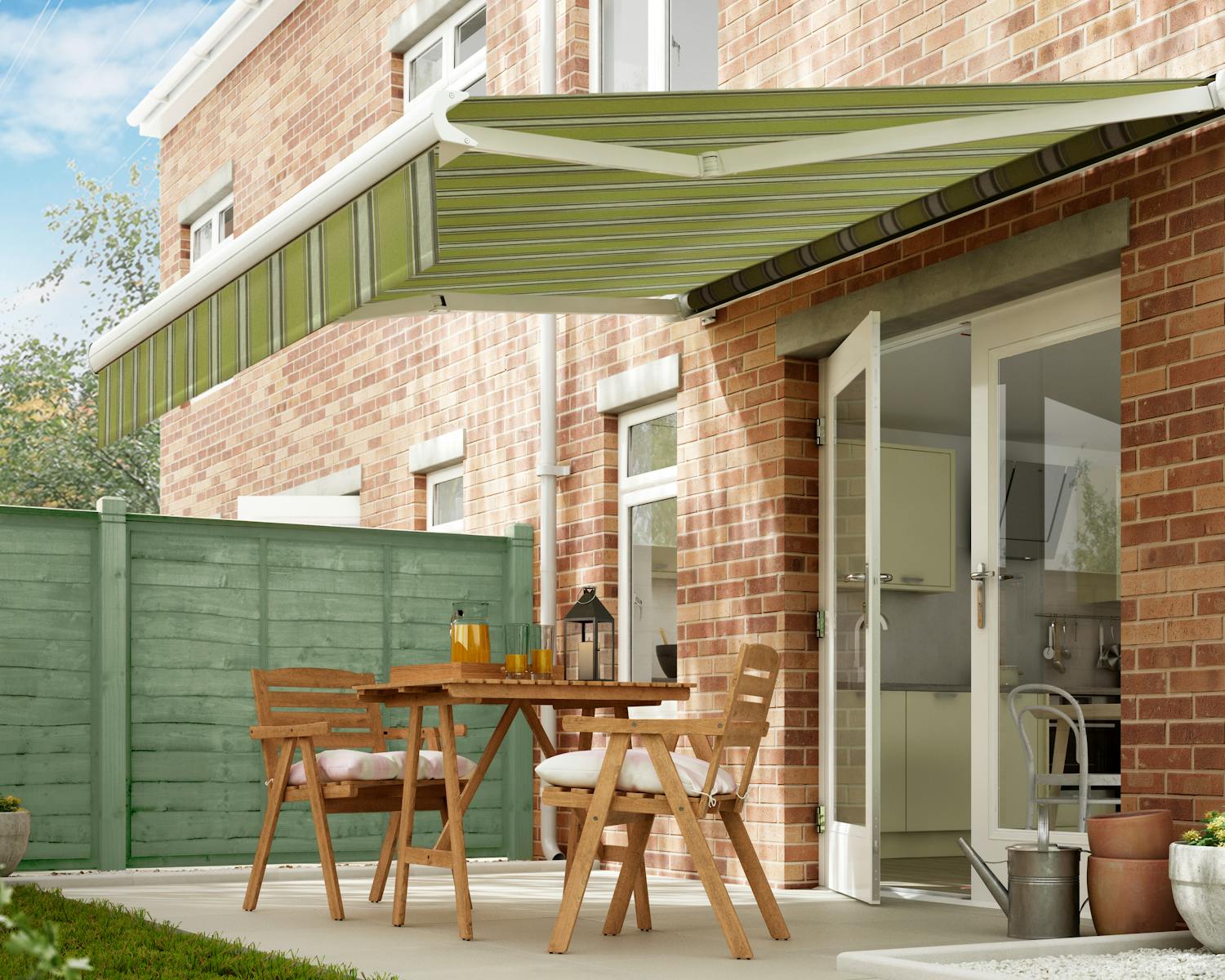 A green retractable awning shades a patio with wooden furniture outside a brick house, near a green fence and garden plants.