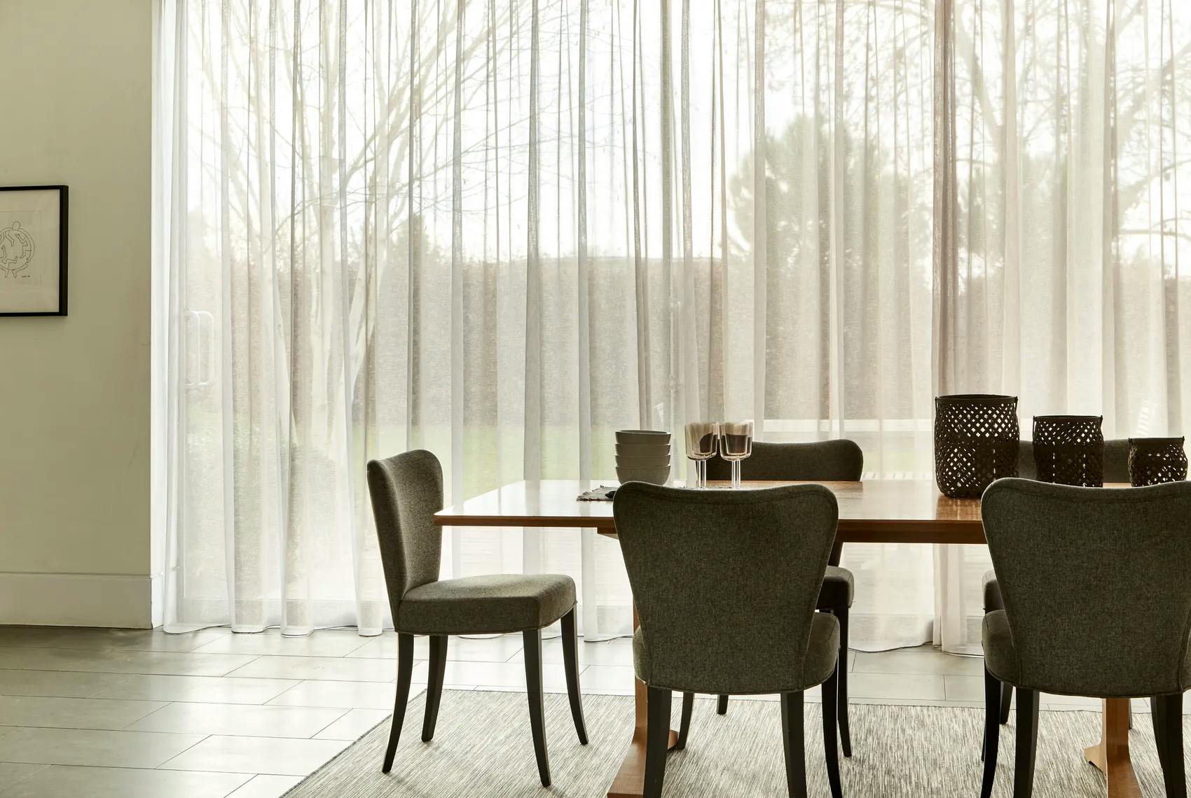 Modern light dining room with white voile curtains on a large window.