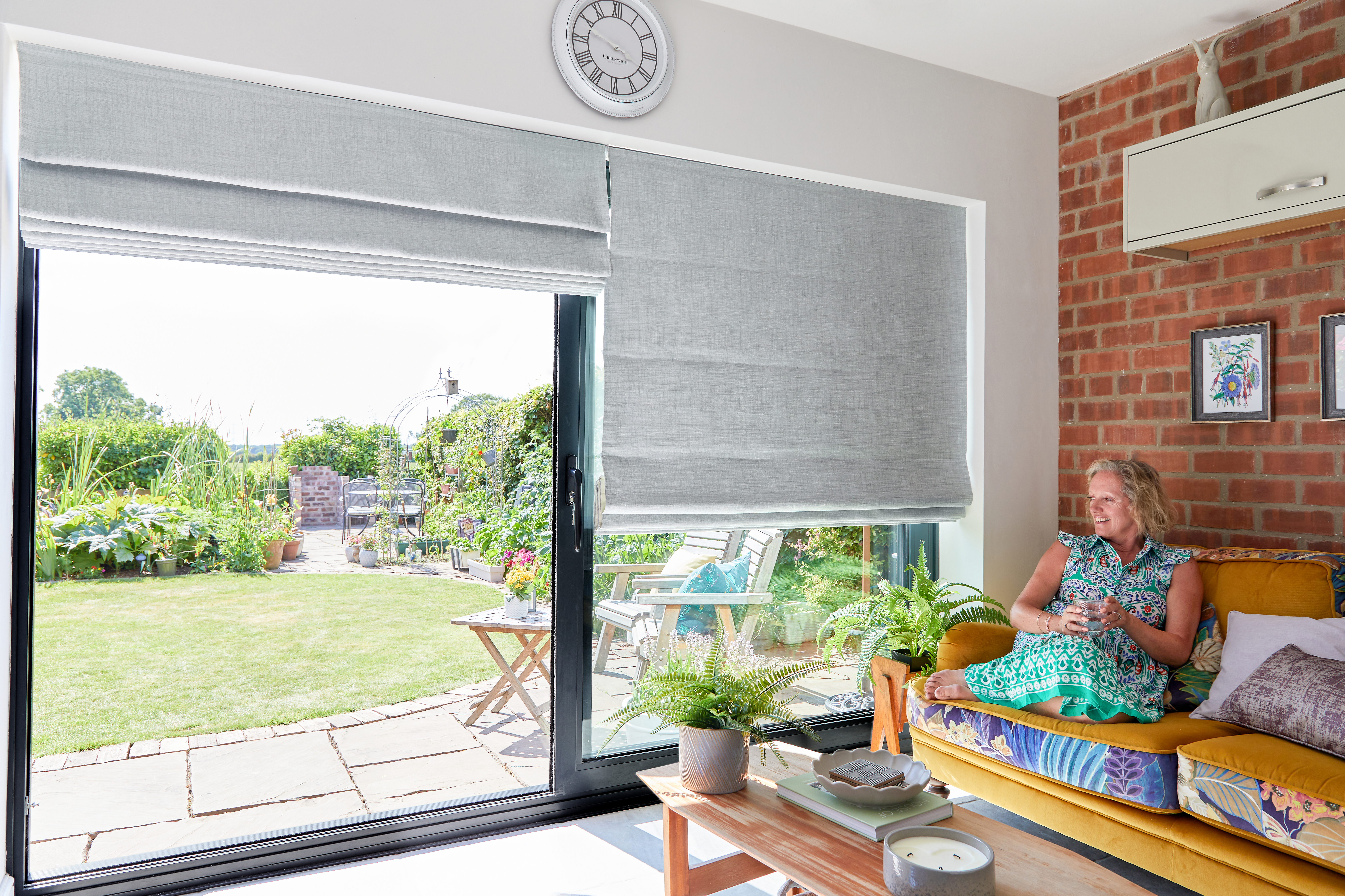 Customer sitting in her home looking out of her patio doors with grey roman blinds on