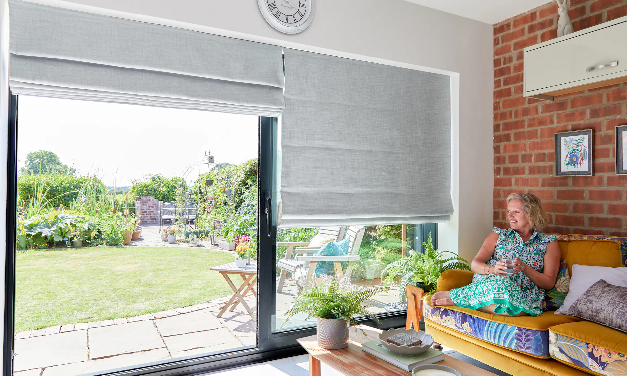 Customer sitting in her home looking out of her patio doors with grey roman blinds on