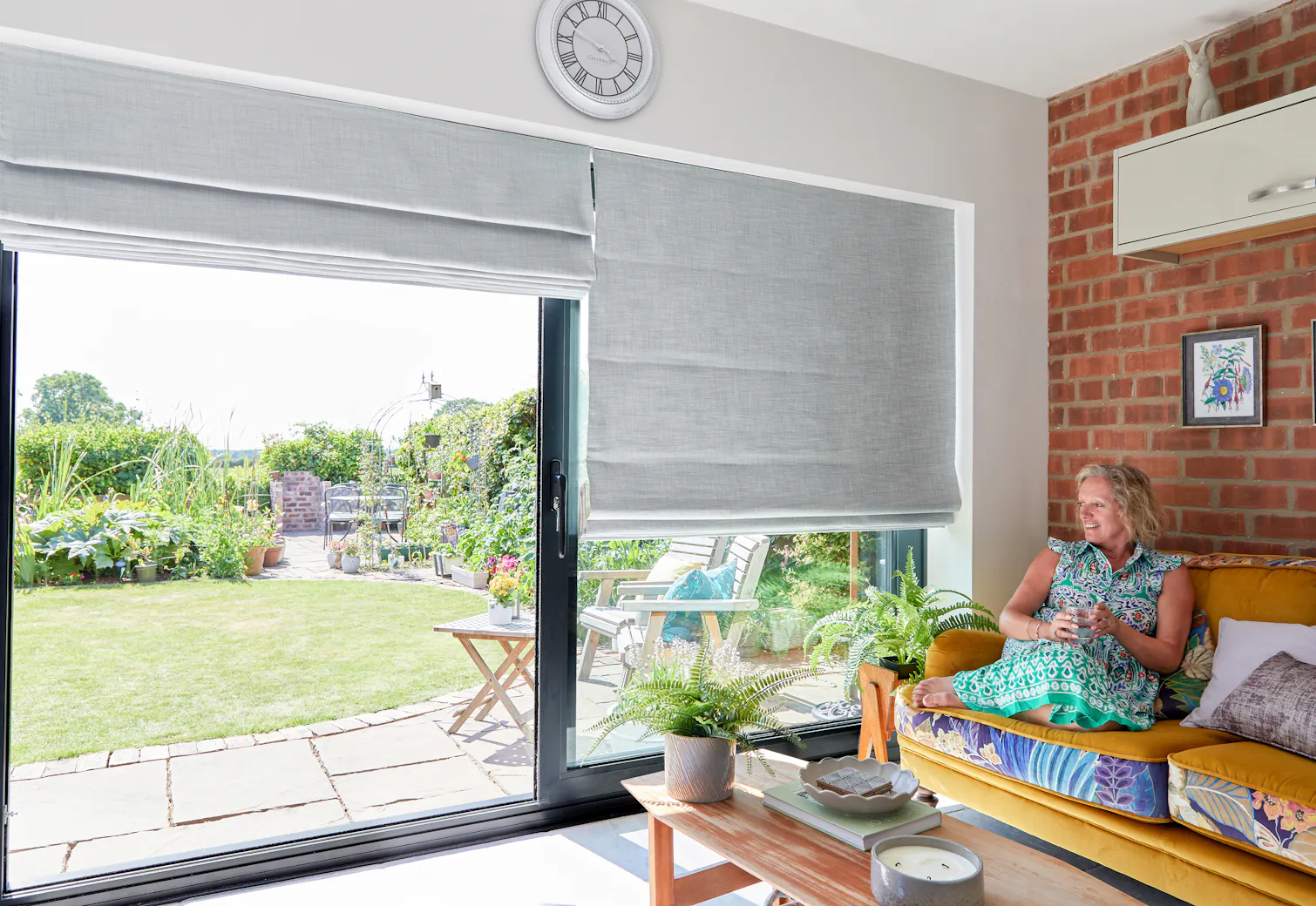Customer sitting in her home looking out of her patio doors with grey roman blinds on