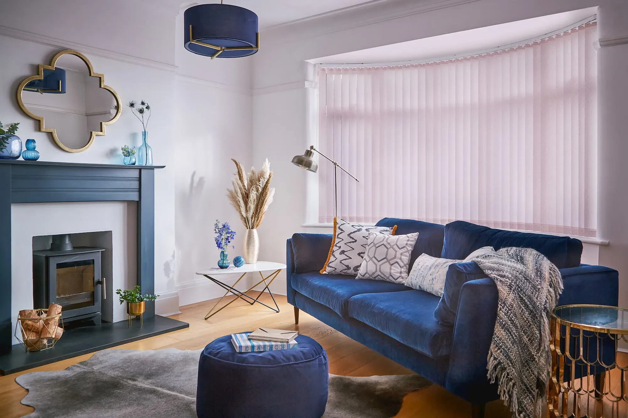 Living room with a bay window dressed in a soft pink blind, filtering daylight behind a blue sofa and complementing modern décor.