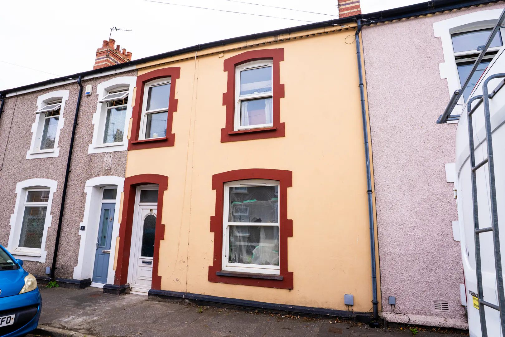 Front of a yellow terraced house with red window frames and a white front door.