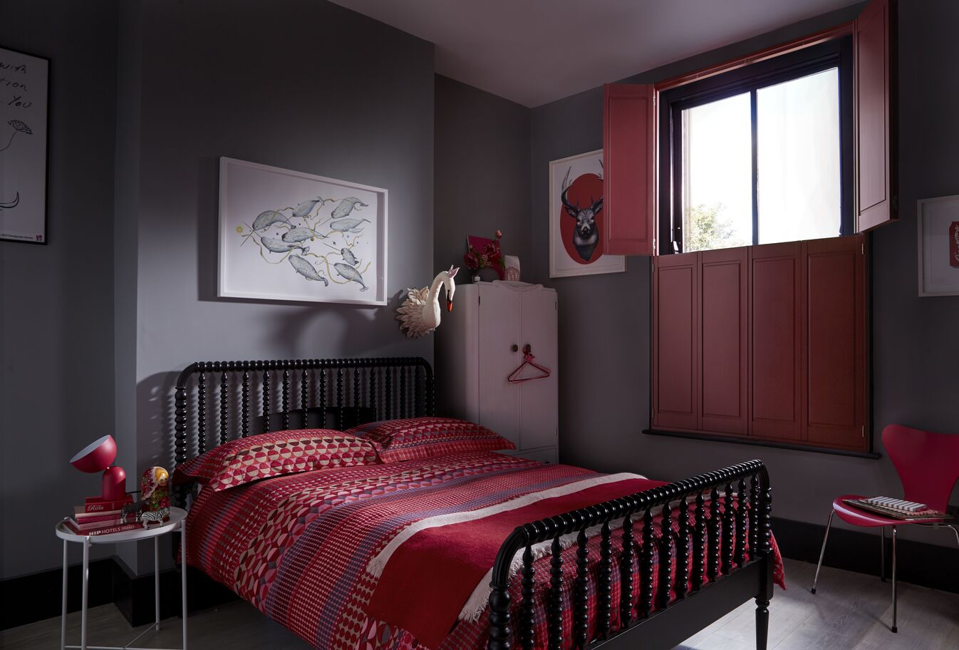 Moody grey bedroom with a black spindle bed, red patterned bedding and deep red shutters on the window.