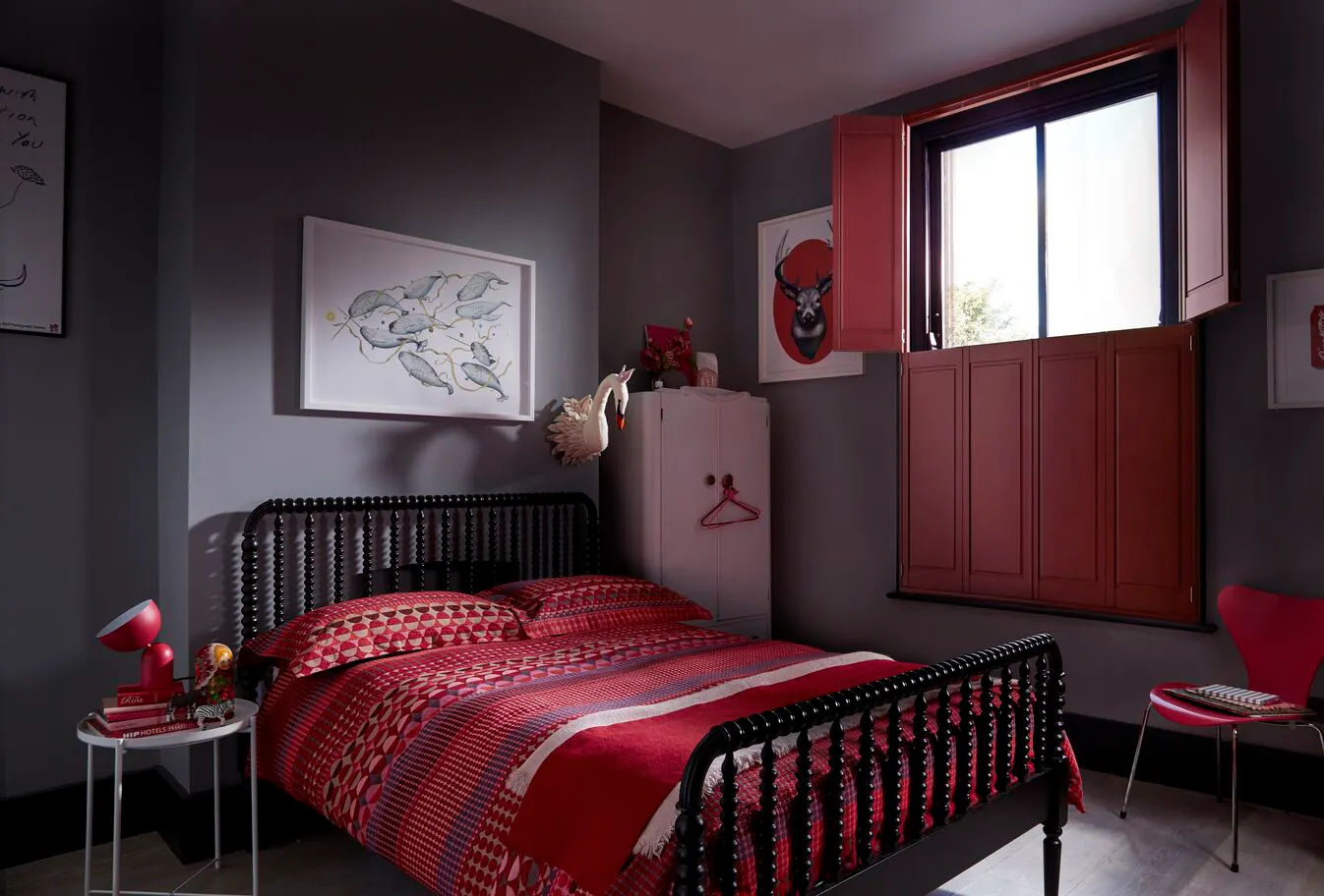 Moody grey bedroom with a black spindle bed, red patterned bedding and deep red shutters on the window.