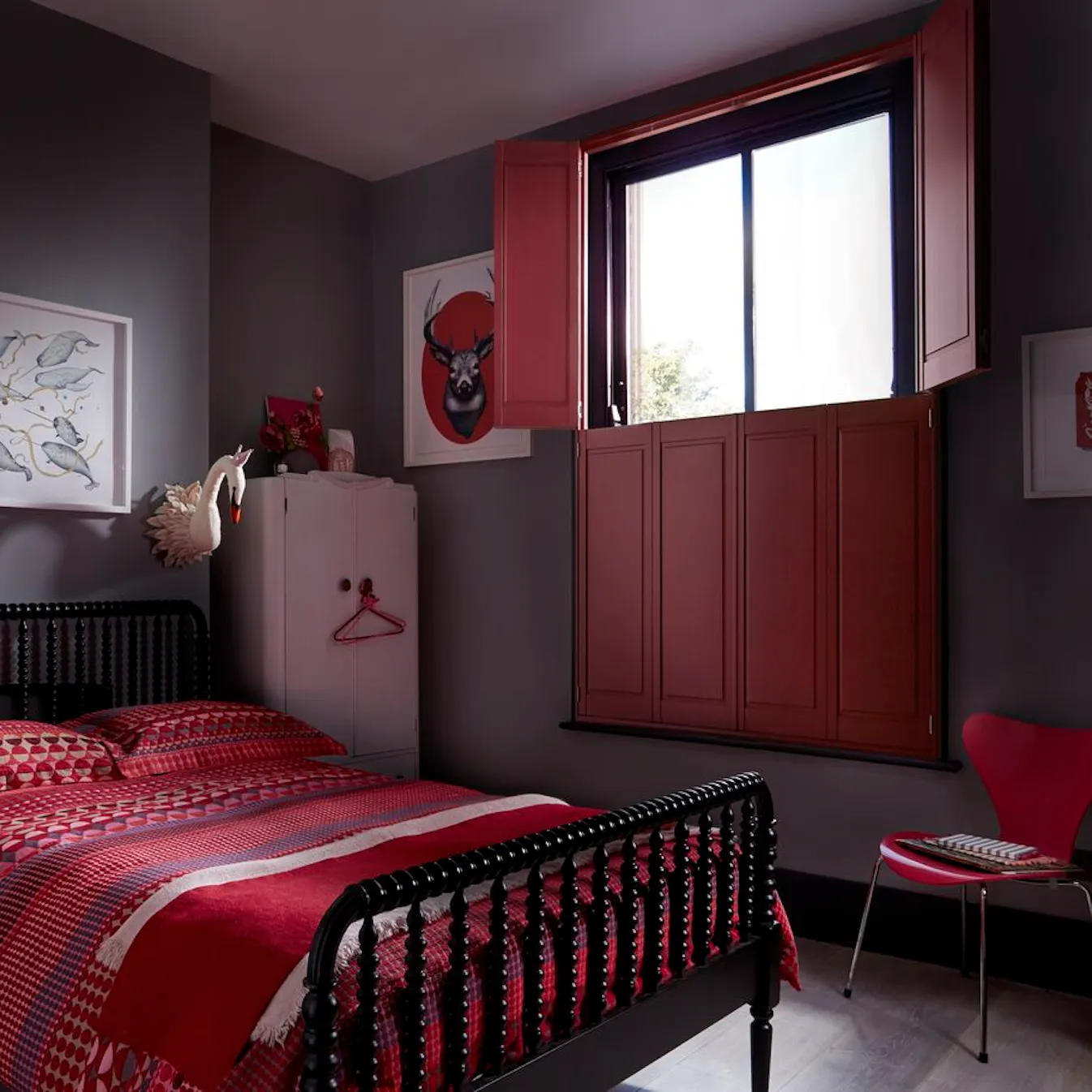 Moody grey bedroom with a black spindle bed, red patterned bedding and deep red shutters on the window.