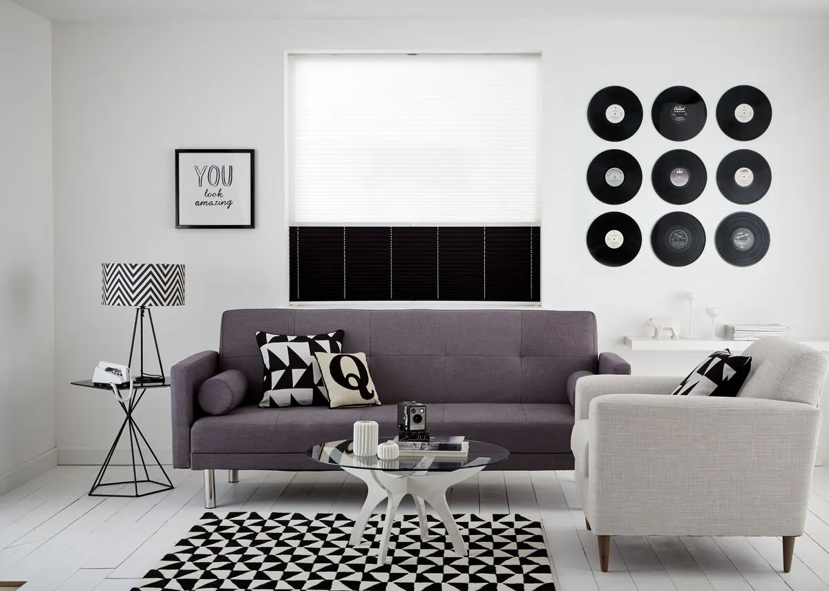 Modern living room with monochrome décor, a grey sofa, geometric cushions and a window with white and black blinds.