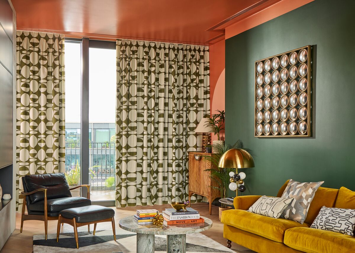 Stylish living room with green patterned curtains, mustard sofa, dark green wall, and mid‑century furniture beneath a coral ceiling.