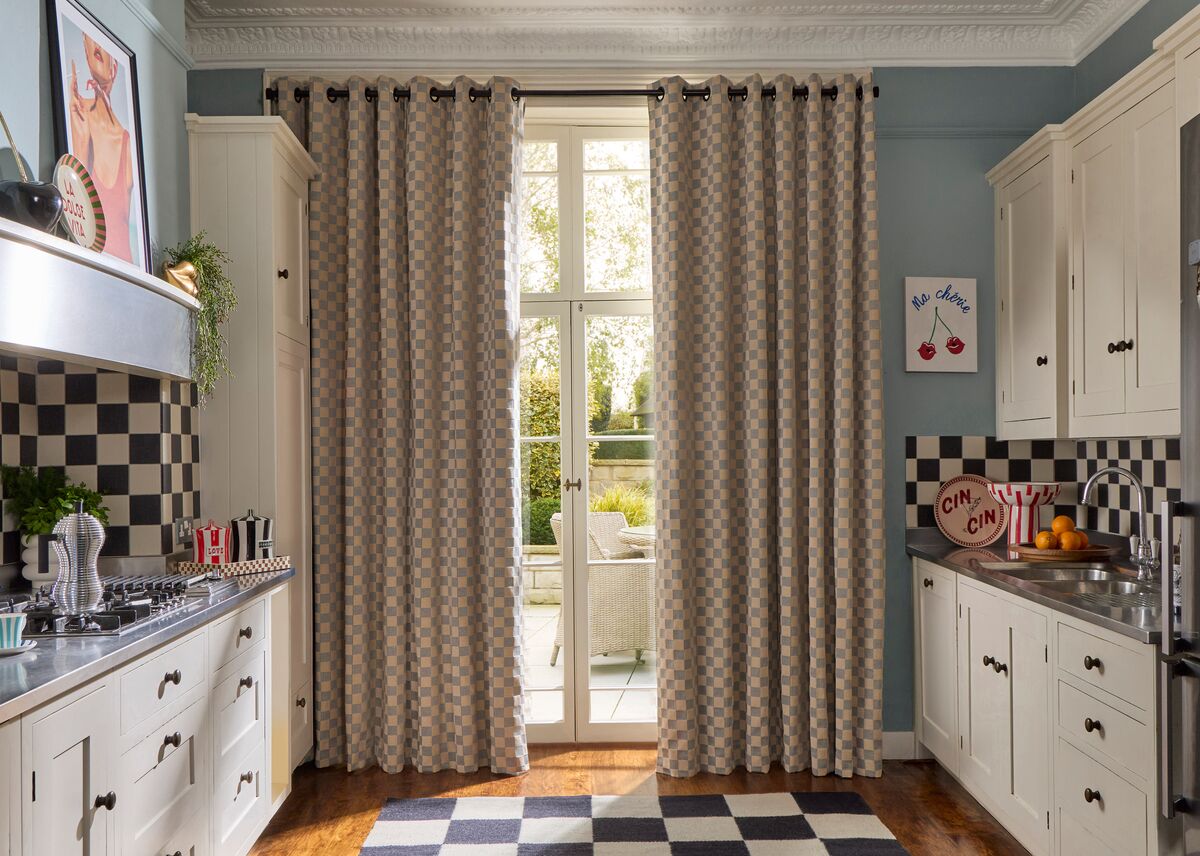 Classic kitchen with checkerboard curtains at French doors, cream cabinets, chequered tiles and a view to a sunlit patio garden.