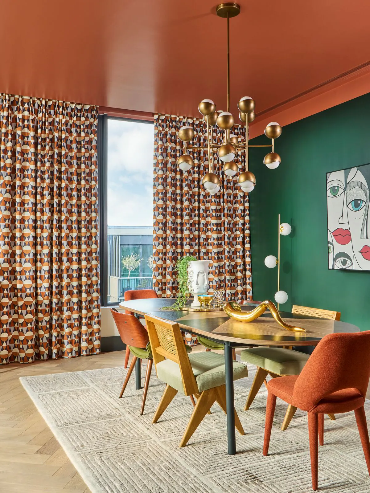 Colourful dining room with patterned amber curtains, a green feature wall, modern chandelier and mid‑century chairs around a dark dining table.