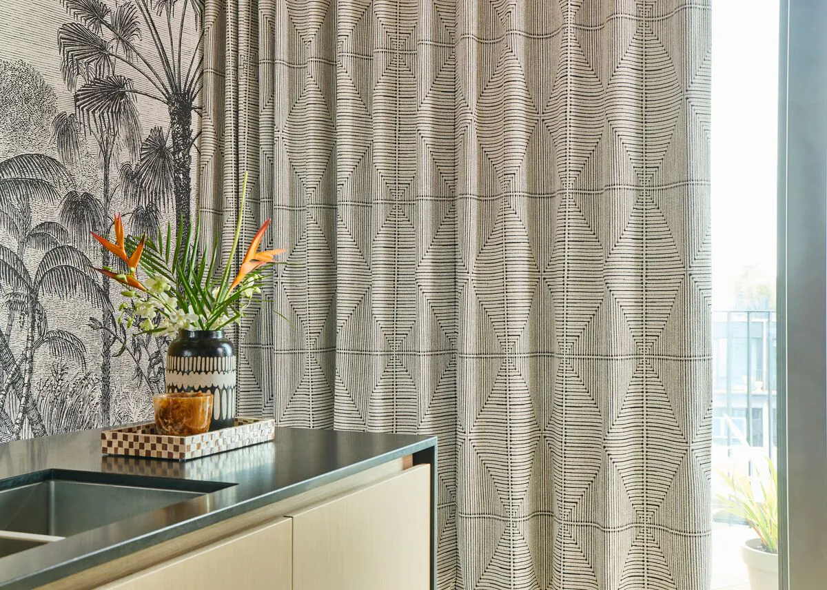 Close-up of a modern interior with geometric patterned curtains, tropical wallpaper and a countertop styled with a vase of flowers.