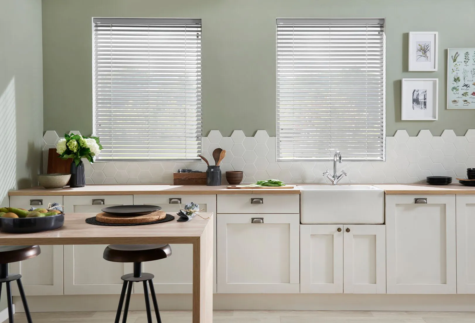 Bright kitchen with two windows featuring white venetian blinds, white cabinets, wooden worktops, and green accents with modern decor.