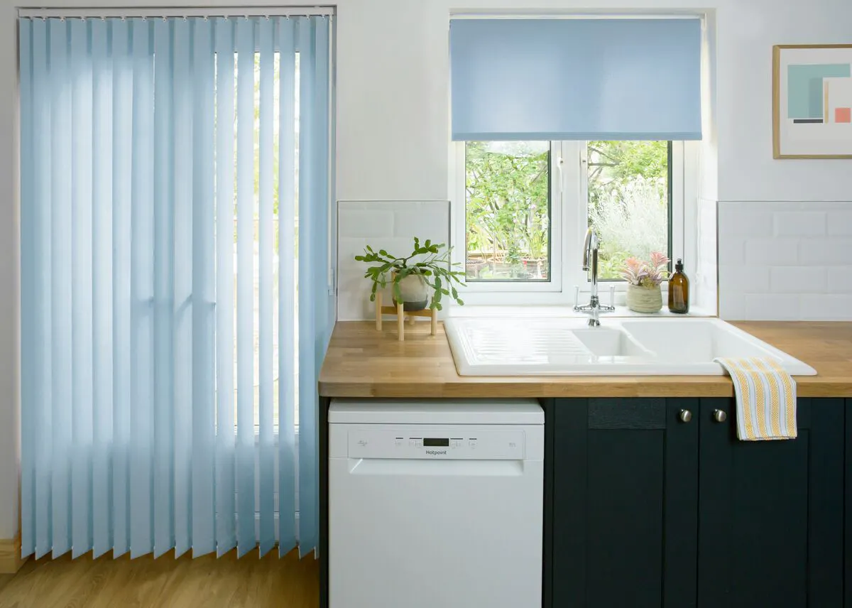 Bright kitchen with pale blue vertical blinds on patio doors and a matching blue roller blind above the sink.