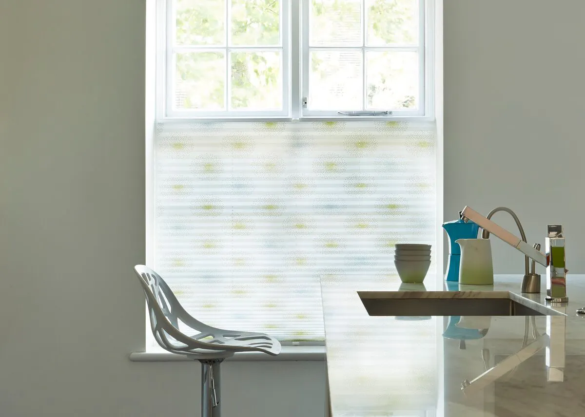 Softly lit kitchen with a patterned pleated blind covering the lower half of a window above a marble counter and modern bar stool.

