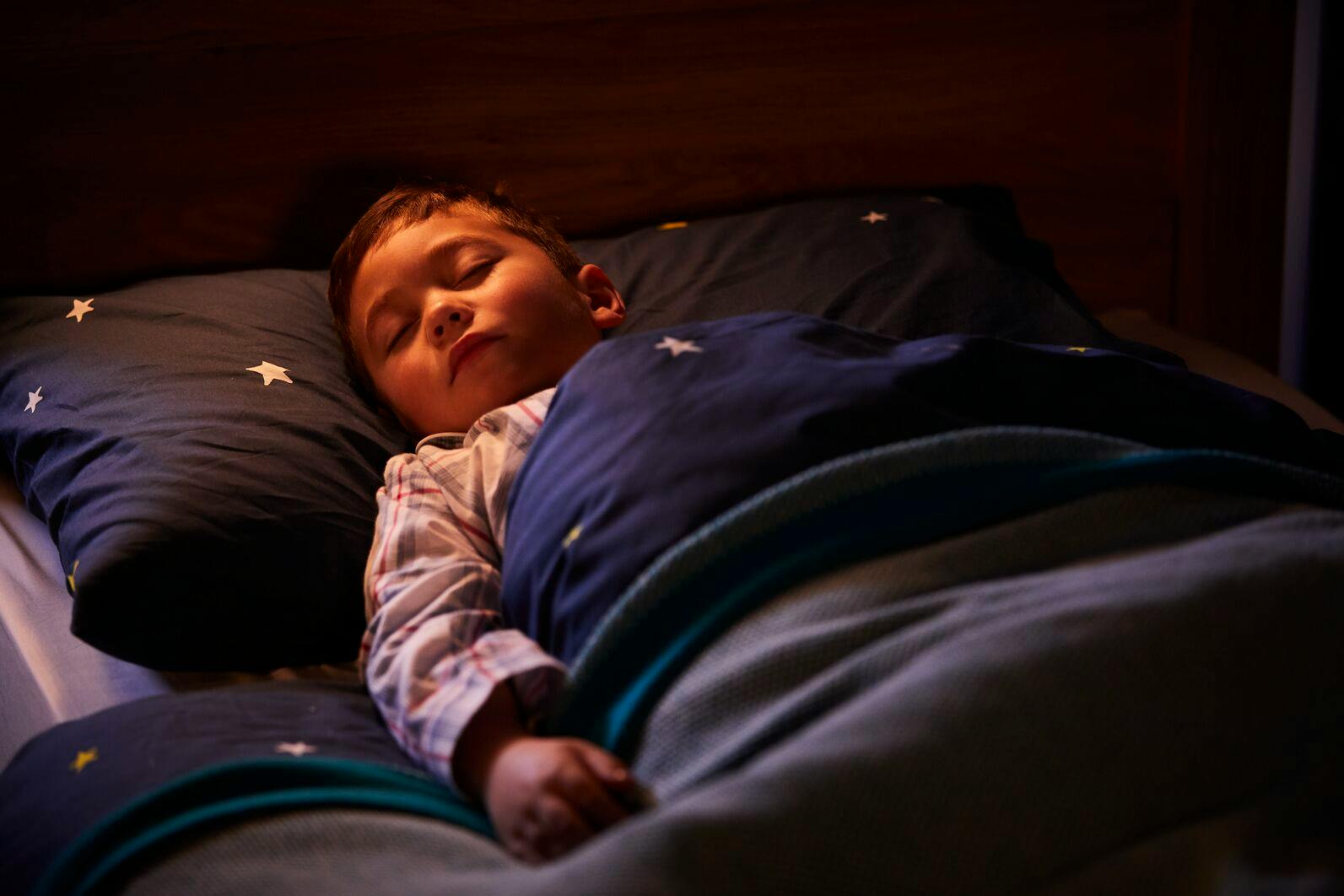A child lying in a dimly lit bedroom under star-patterned bedding.